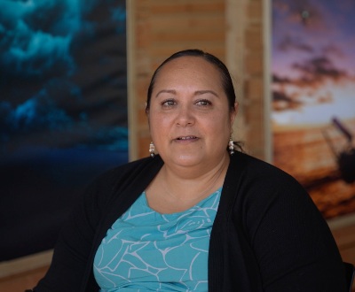 A woman sitting in a room with framed photos of sunsets and the beach.