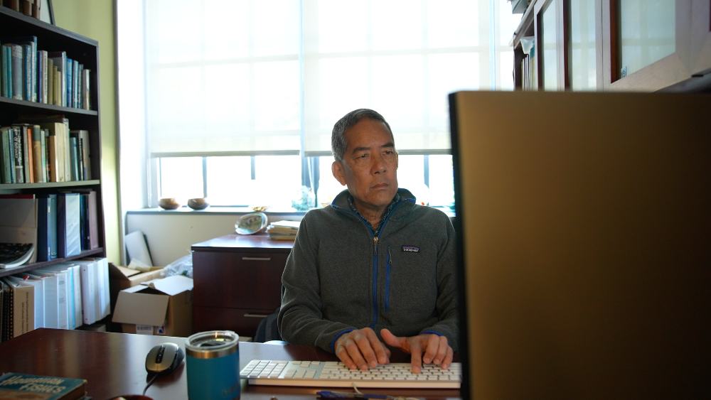 A person sitting at their desk in their office with a computer screen situated in front of them.