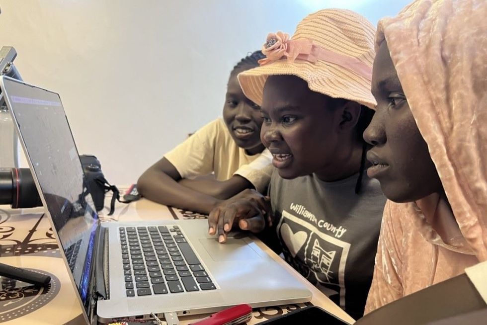 Three young women are working together on a laptop.
