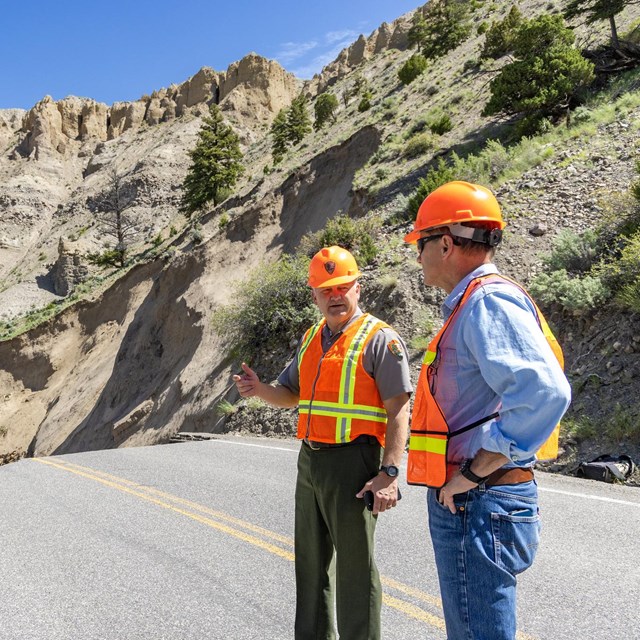 Two people in high-vis gear chatting near a road washout.